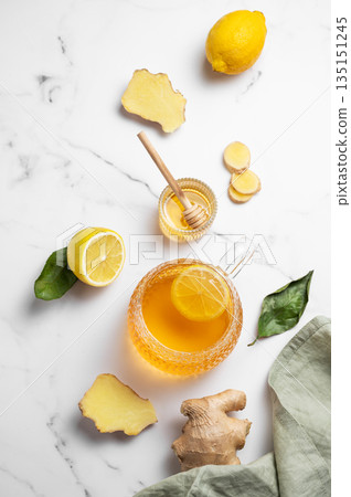 Flat lay of a glass cup of hot tea with fresh lemon and ginger on a light marble background 135151245