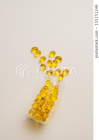 Yellow softgel vitamins capsules scattered in a bottle on a light background. Yellow softgel vitamins capsules scattered in a bottle on a light background. 135151246