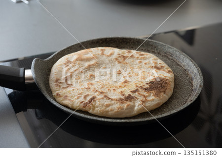 Pita bread cooking in a pan on a modern kitchen Pita bread cooking in a pan on a modern kitchen 135151380