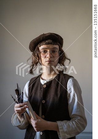 Freelance artist with calm concentrated glance holding canvas, paint brushes, looking at camera Freelance artist with calm concentrated glance holding canvas, paint brushes, looking at camera 135151668