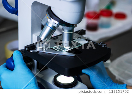 Meticulous observation of sample through microscope in controlled laboratory setting 135151792