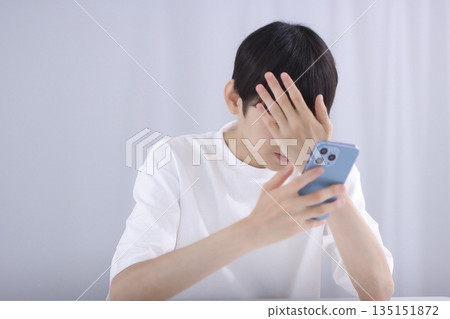A young man looking at his smartphone in the living room and feeling disappointed 135151872