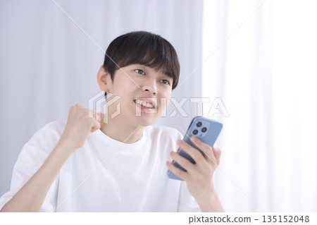 A young man looking at his smartphone in the living room and making a fist pump A young man looking at his smartphone in the living room and making a fist pump 135152048