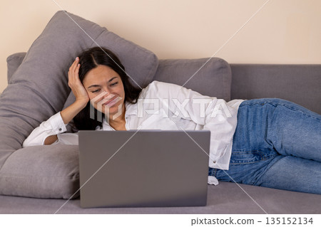 Woman lying on a sofa and working on a laptop. Woman lying on a sofa and working on a laptop. 135152134