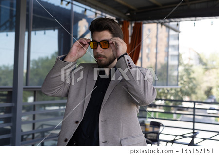 Man in a jacket adjusting his sunglasses outdoors. 135152151
