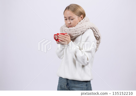 Cold woman wrapped in a scarf holding a red cup. Cold woman wrapped in a scarf holding a red cup. 135152210