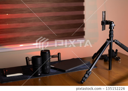 Desk with professional camera lenses and a phone tripod. 135152226