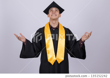 Graduate in a gown and cap gesturing with both hands. 135152242