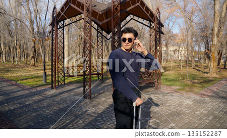 Stylish man with suitcase walking in a sunny autumn park. 135152287