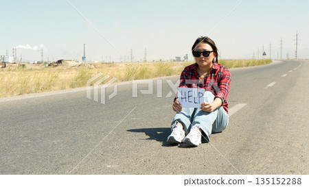 Woman traveler sitting on the side of a road. Woman traveler sitting on the side of a road. 135152288