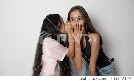 Two girls whispering a secret to each other. 135152309