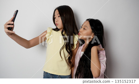 Two young girls taking a selfie together with a phone. 135152317
