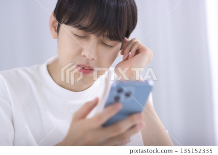 一個年輕人坐在客廳看著他的智慧型手機，感到失望 135152335