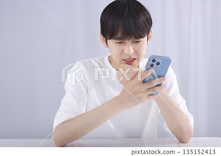 一個年輕人坐在客廳看著他的智慧型手機，感到失望 135152413