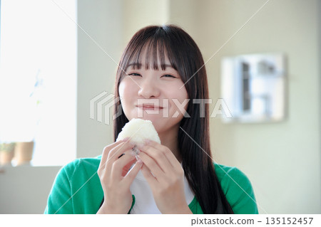 一位年輕女子津津有味地吃著飯糰。 135152457