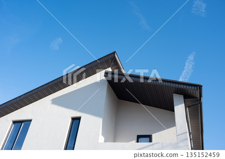 Modern house roof against blue sky with white walls and black corrugated metal roof 135152459