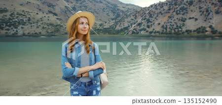 Happy young woman tourist standing on lake with mountains background. Greece, island Crete Happy young woman tourist standing on lake with mountains background. Greece, island Crete 135152490
