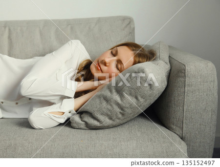 Happy relaxed young woman sleeping lying on the couch on gray soft pillow in living room at home 135152497