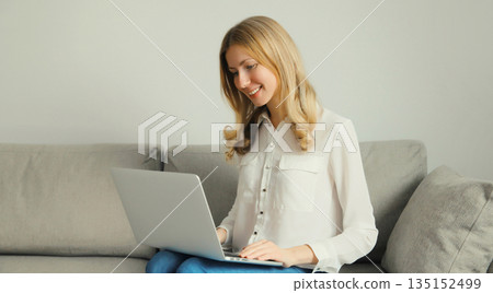 Happy modern woman working with laptop, freelancer girl sitting on a couch in the living room 135152499