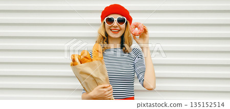 Happy cheerful smiling young woman holding grocery shopping paper bag with white bread baguette 135152514