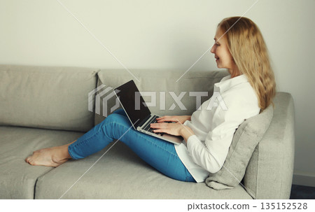 Happy modern woman working with laptop, freelancer girl sitting on a couch in the living room Happy modern woman working with laptop, freelancer girl sitting on a couch in the living room 135152528