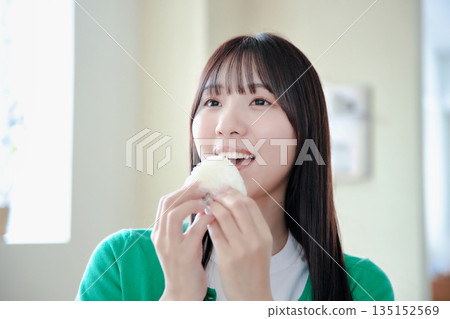一位年輕女子津津有味地吃著飯糰。 一位年輕女子津津有味地吃著飯糰。 135152569