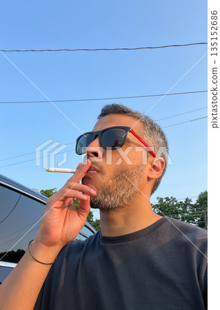A man is smoking a cigarette while wearing sunglasses A man is smoking a cigarette while wearing sunglasses 135152686