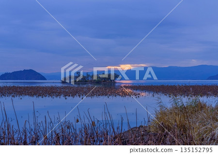 The afterglow of the sunset reflected on the lake surface and the marshland of withered lotus flowers: the tranquil nature of Japan in late autumn The afterglow of the sunset reflected on the lake surface and the marshland of withered lotus flowers: the tranquil nature of Japan in late autumn 135152795