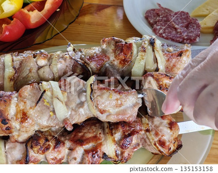 A close-up of grilled pork with onions on skewers. Family dinner al fresco. A close-up of grilled pork with onions on skewers. Family dinner al fresco. 135153158