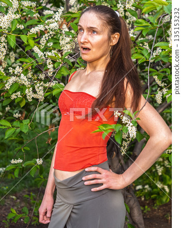 Young woman sneezes in the park against the background of a flowering tree. Allergy to pollen concept. Young woman sneezes in the park against the background of a flowering tree. Allergy to pollen concept. 135153232