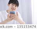 A young man looking at his smartphone in the living room and making a fist pump A young man looking at his smartphone in the living room and making a fist pump 135153474