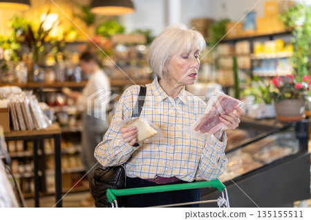 Elderly woman choosing cheese and bacon in grocery supermarket Elderly woman choosing cheese and bacon in grocery supermarket 135155511