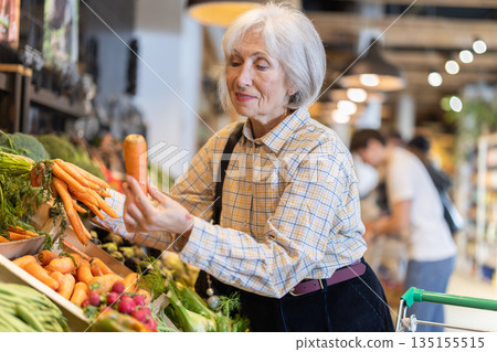 Elderly woman chooses carrots in grocery supermarket Elderly woman chooses carrots in grocery supermarket 135155515
