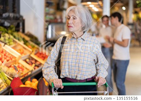 In food store, senior woman with trolley looking for something on shelf of showcase 135155516