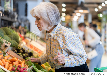 In cozy self-service store, senior woman customer takes tomatoes out of box 135155517
