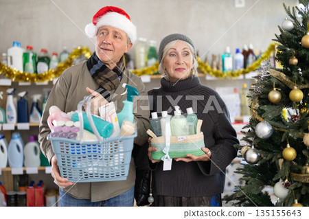 On New Year Eve, senior couple in store with full shopping cart and gift set of cosmetics 135155643