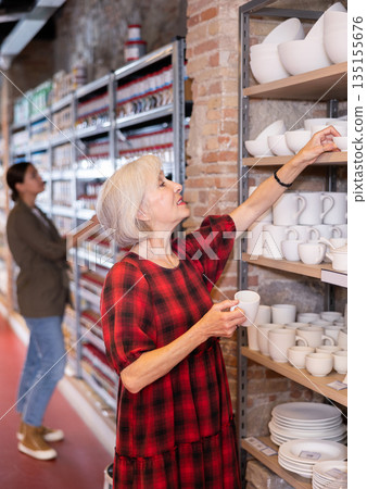 Elderly woman chooses pottery clay cup Elderly woman chooses pottery clay cup 135155676