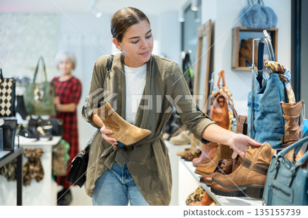 Interested young woman choosing comfortable fall footwear in shoe store Interested young woman choosing comfortable fall footwear in shoe store 135155739