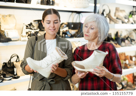 Two female shoppers discussing models of winter boots in shoe store Two female shoppers discussing models of winter boots in shoe store 135155779