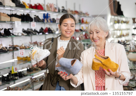 Two women happily discuss choice of modern leather sandals with platform or sneakers Two women happily discuss choice of modern leather sandals with platform or sneakers 135155797