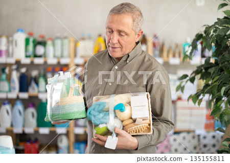 Senior man studies label and choose shower cosmetic present, packaged in basket. Senior man studies label and choose shower cosmetic present, packaged in basket. 135155811