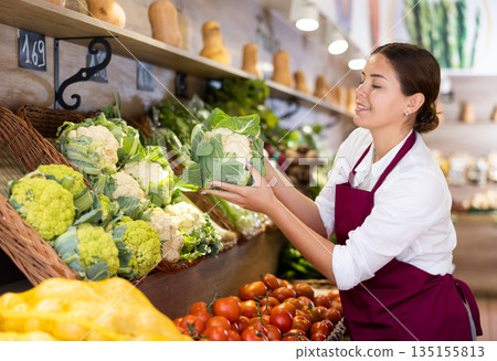 Young saleswoman laying out fresh cauliflower on produce display Young saleswoman laying out fresh cauliflower on produce display 135155813