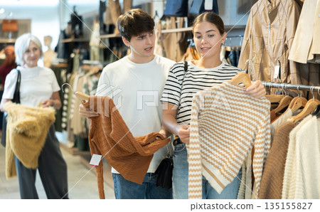 Young girl consults with male friend about purchasing sweater during shopping Young girl consults with male friend about purchasing sweater during shopping 135155827