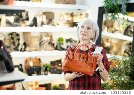Elderly woman chooses handbag in store Elderly woman chooses handbag in store 135155828