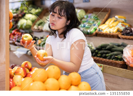 Young asian girl choosing ripe apples on store display 135155850