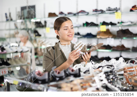 Young woman chooses sandals in shoe store Young woman chooses sandals in shoe store 135155854