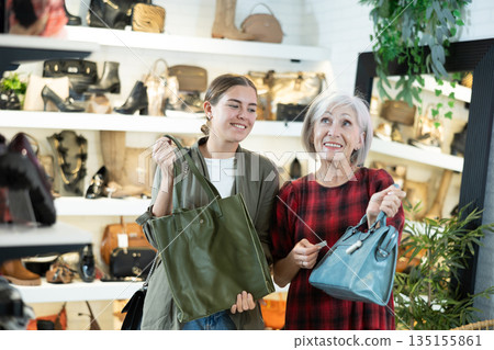 Two cheerful female shoppers discussing models of handbags in store Two cheerful female shoppers discussing models of handbags in store 135155861