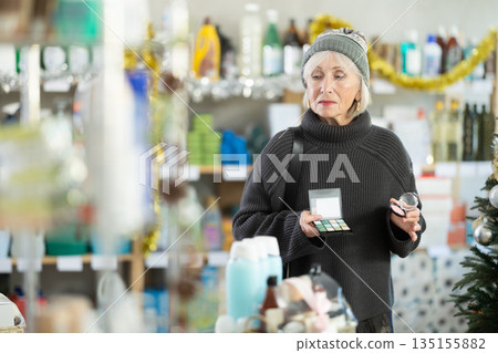 Elderly woman chooses cosmetics and eye shadow in supermarket before Christmas Elderly woman chooses cosmetics and eye shadow in supermarket before Christmas 135155882