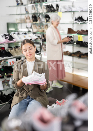 Young satisfied woman trying on new sneakers in shoe store Young satisfied woman trying on new sneakers in shoe store 135156039