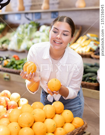 Delighted young woman purchaser choosing oranges in grocery store Delighted young woman purchaser choosing oranges in grocery store 135156045